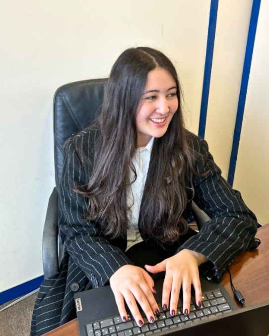 Graduate apprenticeships law learner smiling while typing at a desk, representing workplace-based legal training and professional development.